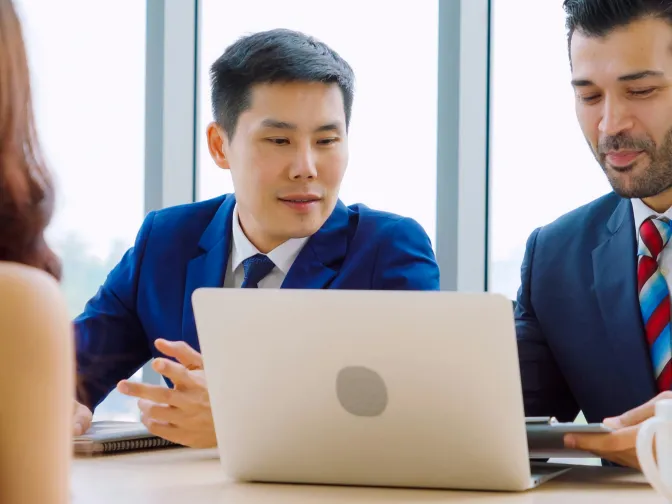 Colleagues discussing work around a laptop in a meeting room