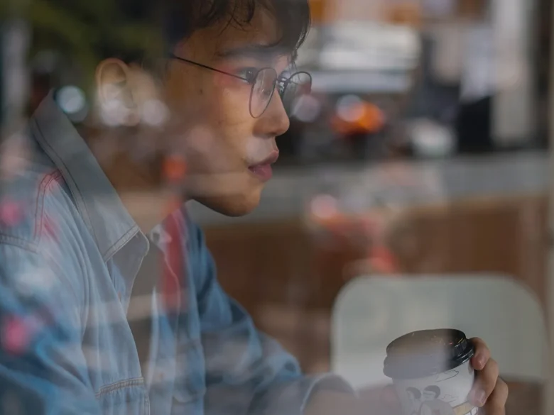 Man in a denim shirt at a cafe window, the street reflected across the glass