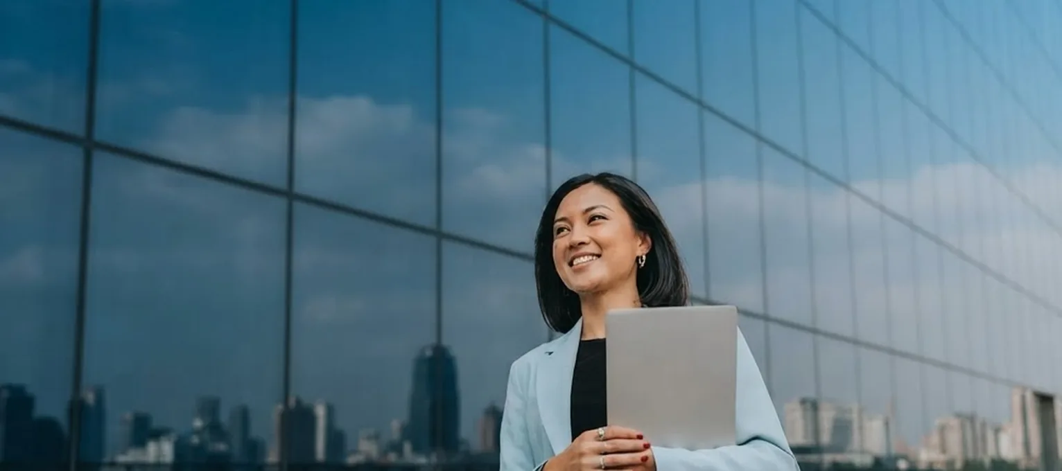 Executive holding a laptop outside a glass tower, the skyline reflected behind her